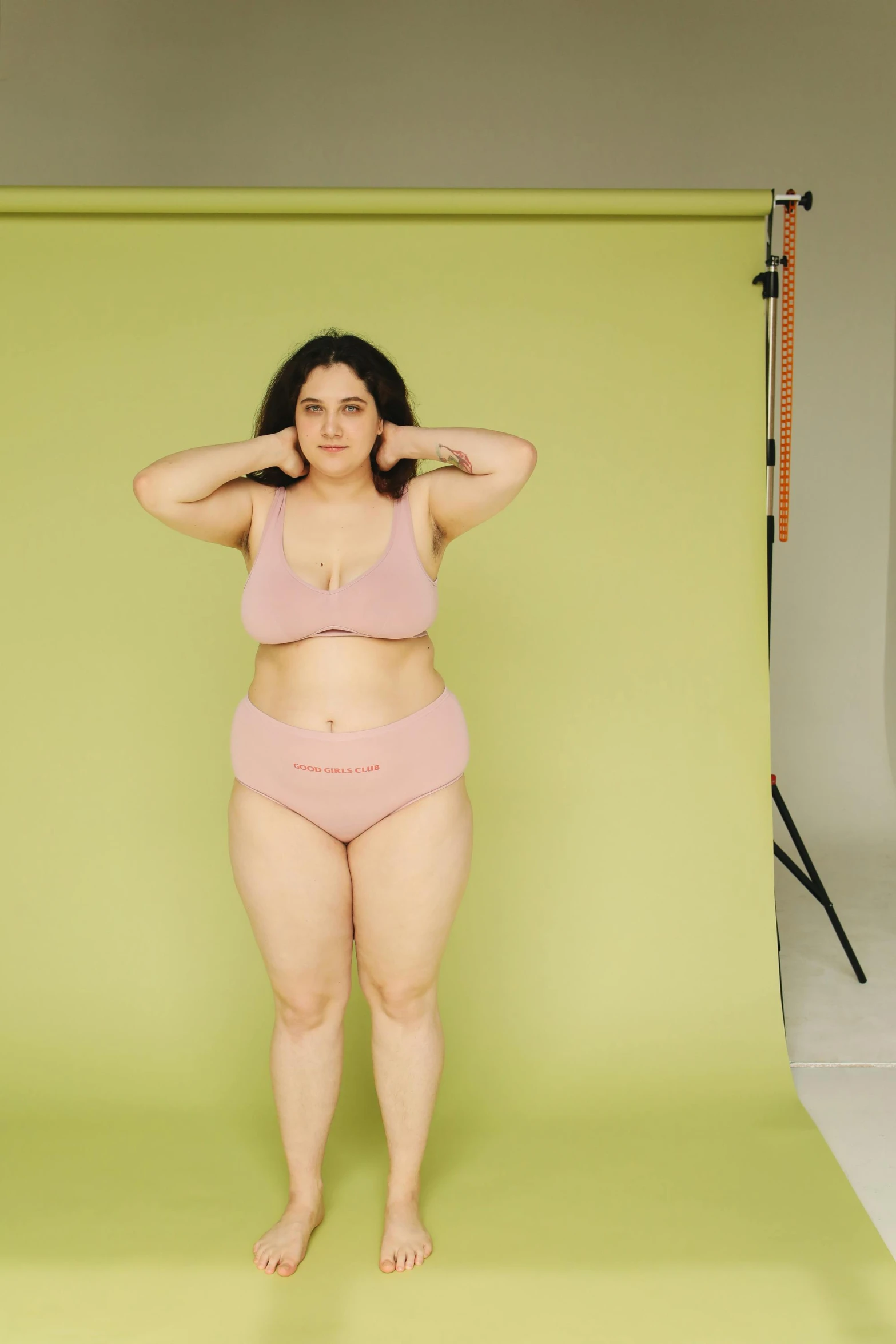 a woman standing in front of a green screen, pale pink bikini, rubenesque, non binary model, on a gray background