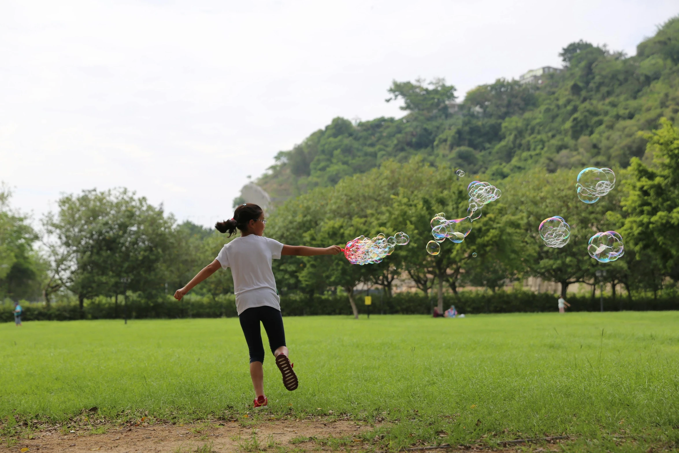 a young girl running across a lush green field, by david rubín, pexels contest winner, process art, soap bubbles, sangyeob park, thawan duchanee, with a park in the background