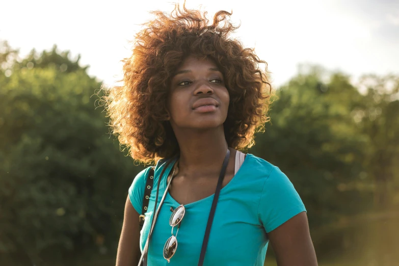 a woman standing in a field with a camera, by Lily Delissa Joseph, pexels contest winner, natural hair, teal, backlit face, ( brown skin )