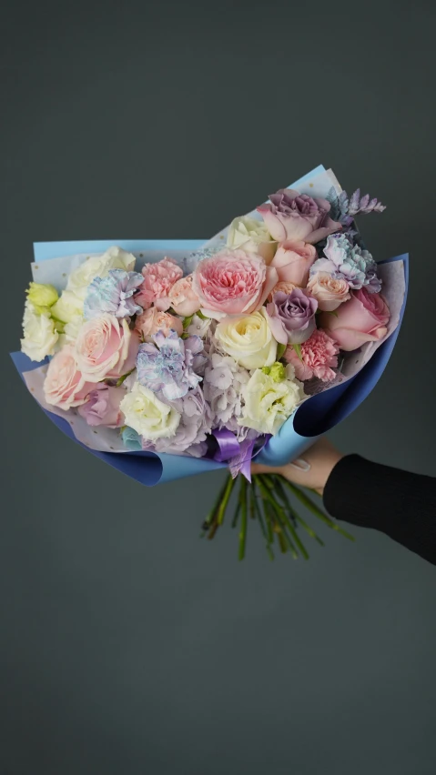 a person holding a bouquet of flowers in their hand, a pastel, inspired by François Boquet, unsplash, on a gray background, pastel blues and pinks, very large, made of flowers