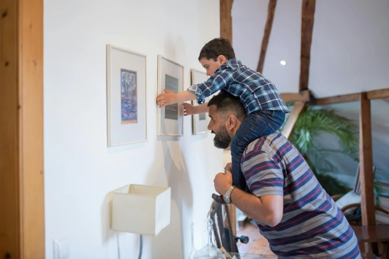 a man and a child hanging pictures on a wall, by Dan Content, pexels contest winner, visual art, square pictureframes, natural lighting, printmaking, animation still