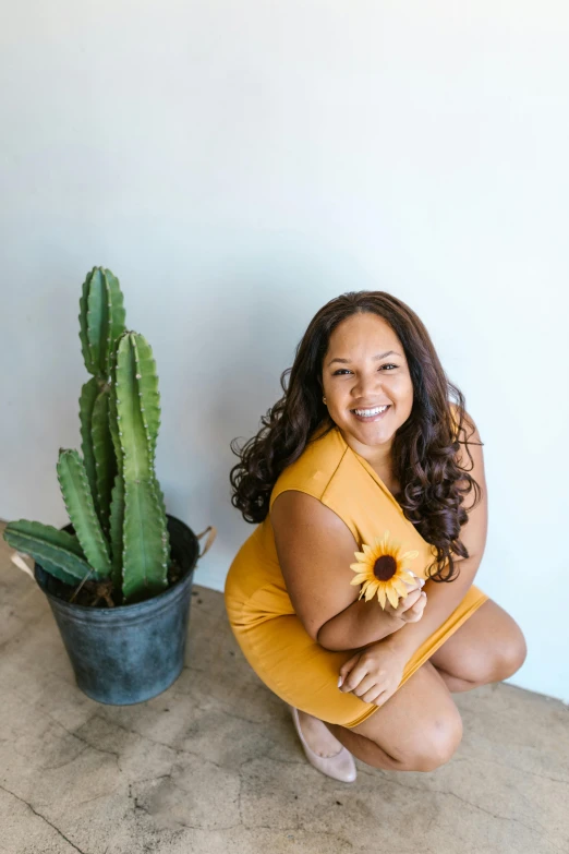 a woman sitting on top of a cement floor next to a cactus, wavy hair yellow theme, alanis guillen, smiling down from above, sunflowers in the background