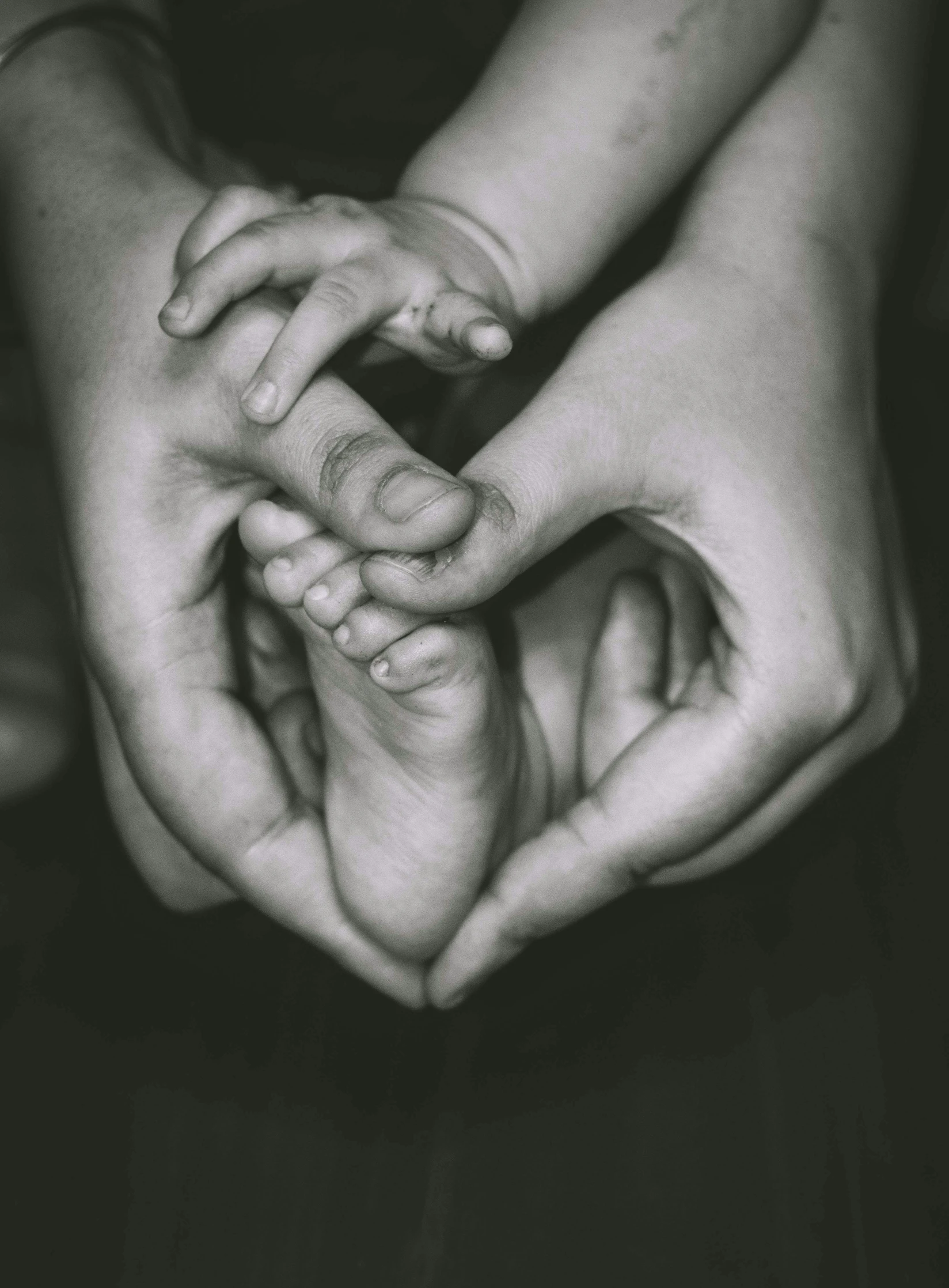 a black and white photo of a person holding a baby's hand, pexels contest winner, symbolism, barefeet, sepia toned, multi-part, high quality product image”