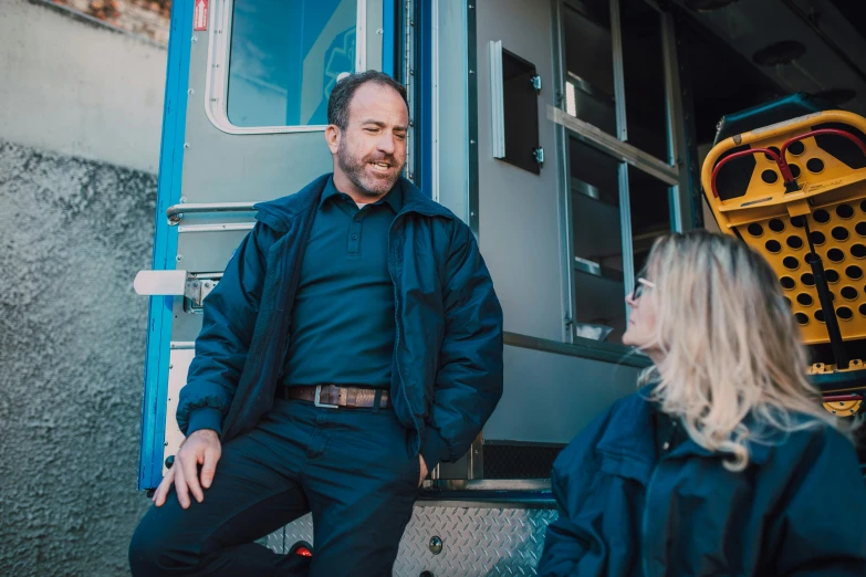 a man and a woman standing in front of a truck, by Harriet Zeitlin, pexels, paul giamatti, sitting down casually, emergency, profile image