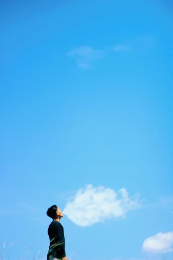 a man standing on top of a grass covered field, a picture, unsplash, minimalism, cloudless blue sky, rinko kawauchi, on a rooftop, low-angle