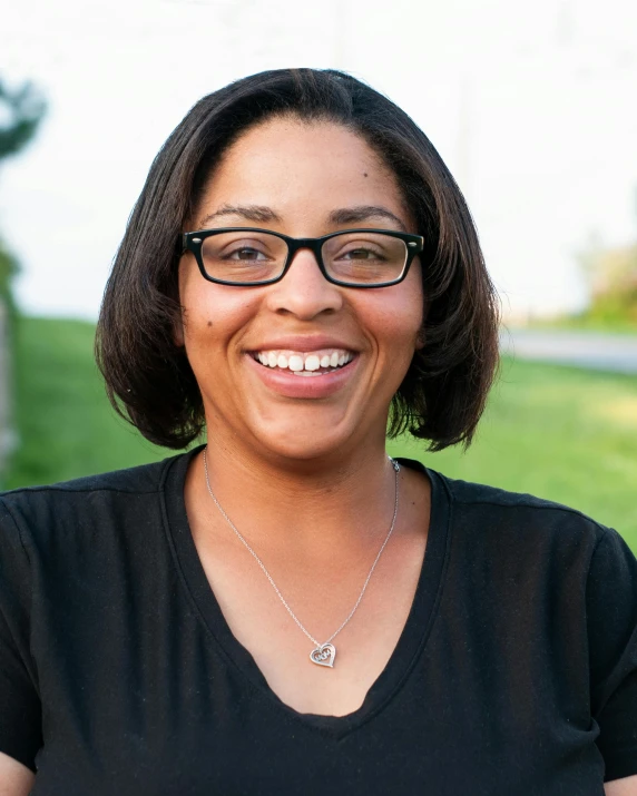 a woman with glasses smiling at the camera, by Washington Allston, with a park in the background, alexis franklin, profile image, dim lit