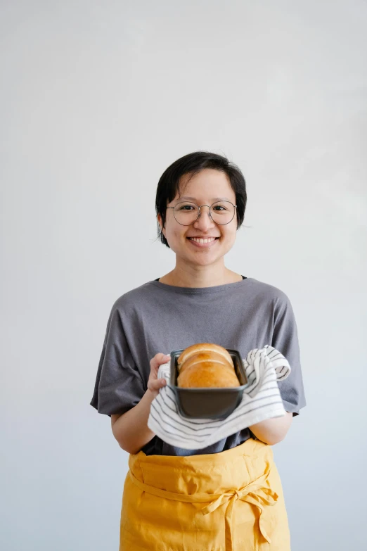 a woman in an apron holding a loaf of bread, inspired by Ruth Jên, pexels contest winner, mingei, wearing an orange t-shirt, steamed buns, headshot, slightly minimal