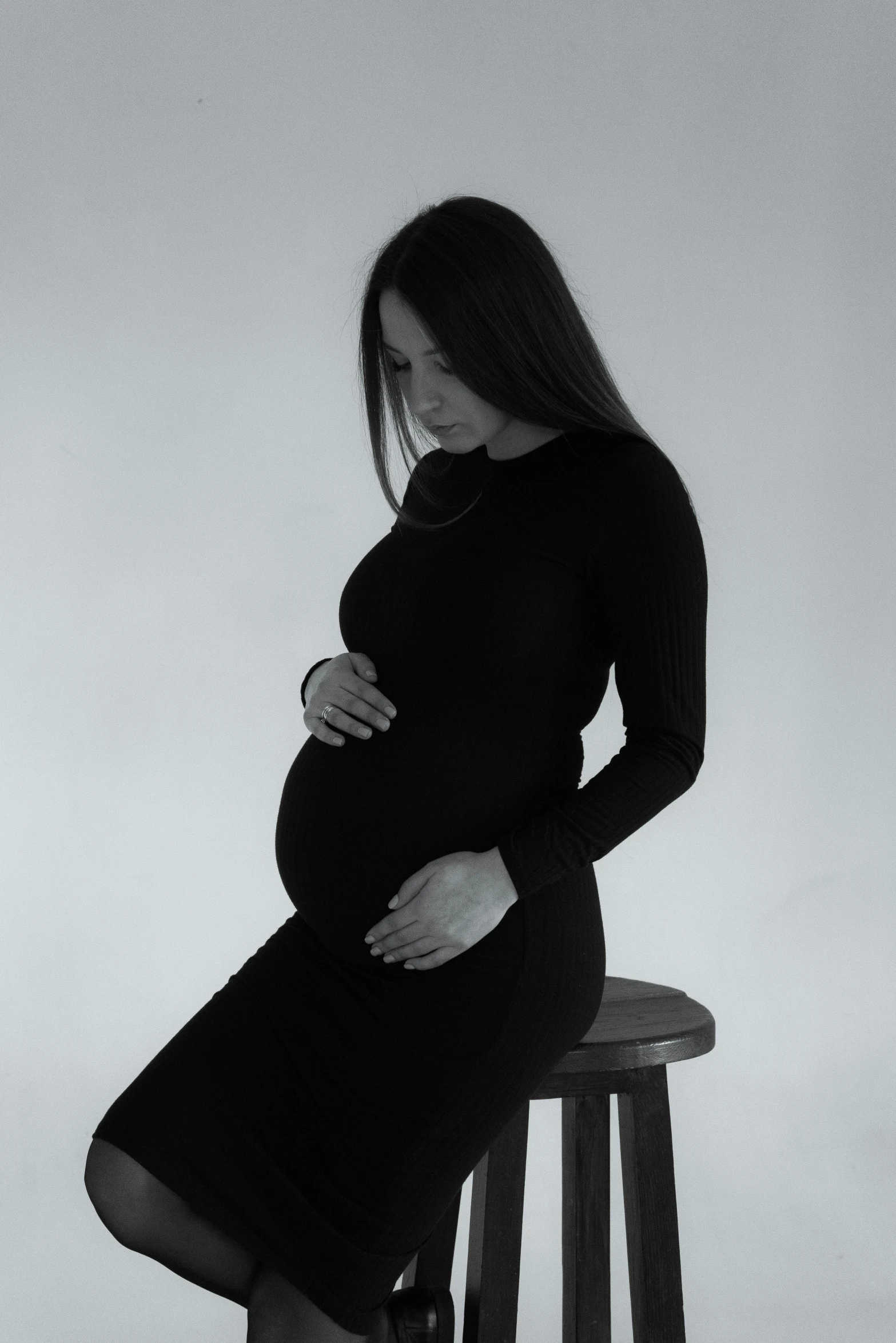 a pregnant woman is sitting on a stool, by Clifford Ross, pexels contest winner, symbolism, black outfit, profile image, woman with black hair, instagram post