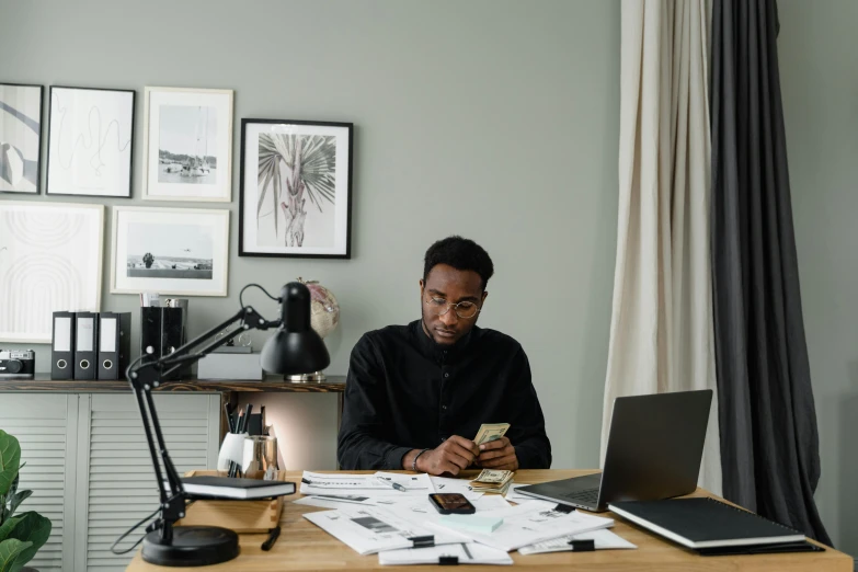 a man sitting at a desk in front of a laptop, by Carey Morris, pexels contest winner, looking at his phone, black man, professional drawing, busy room