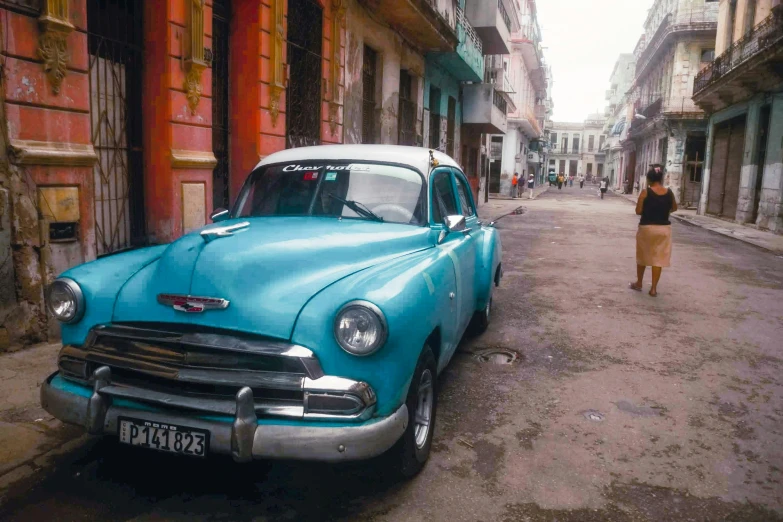 a blue car parked on the side of a street, by Tom Wänerstrand, 30-year-old woman from cuba, in a city with a rich history, 🕹️ 😎 🔫 🤖 🚬, colorful”