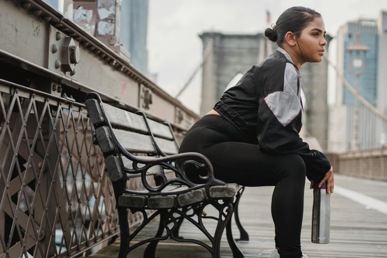 a woman sitting on a bench on a bridge, trending on pexels, chappie in an adidas track suit, black ponytail, gritty image, fit curvy physique