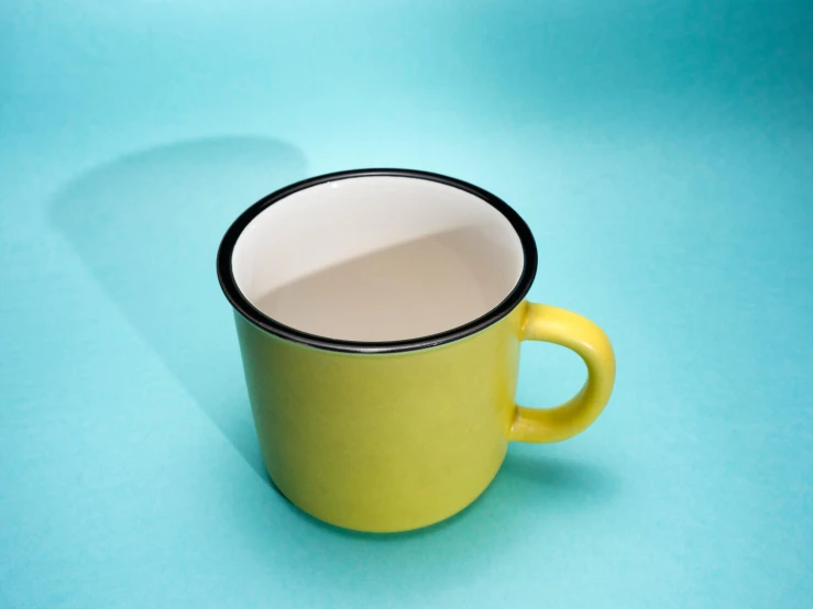 a yellow cup sitting on top of a blue surface, by Doug Ohlson, unsplash, enamel, yellow and black trim, green tea, mug shot