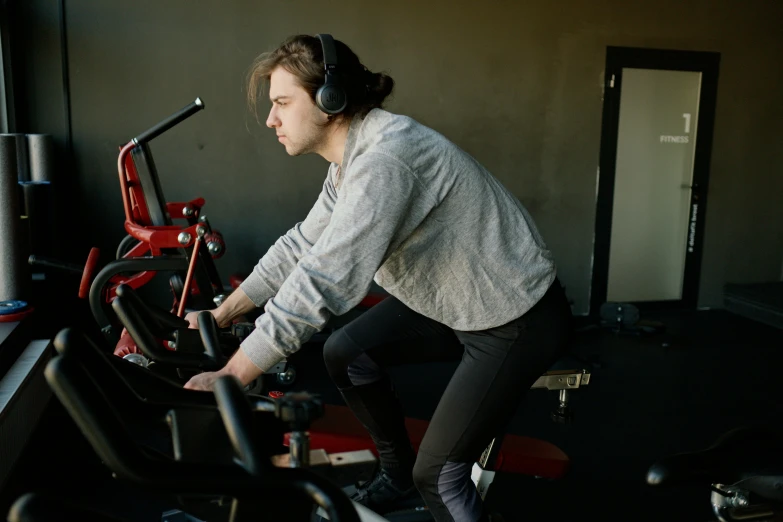 a man riding a stationary bike in a gym, by Emma Andijewska, pexels contest winner, hurufiyya, with head phones, avatar image, bent over posture, high quality image