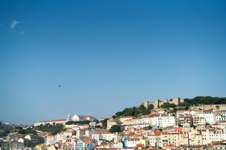 a group of people standing on top of a beach next to a body of water, inspired by Almada Negreiros, pexels contest winner, renaissance, city on a hillside, clear blue sky, square, aircraft