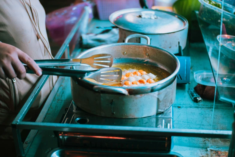 a person cooking food in a pan on a stove, a still life, pexels contest winner, teal and orange colours, stainless steel, polka dot, food stall