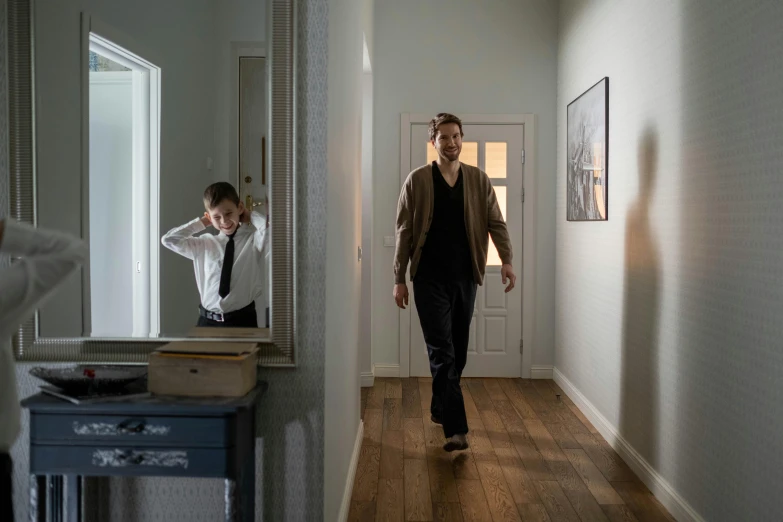 a man walking down a hallway next to a mirror, a picture, denis villeneuve movie still, hammershøi, at home, taken with sony a7r camera