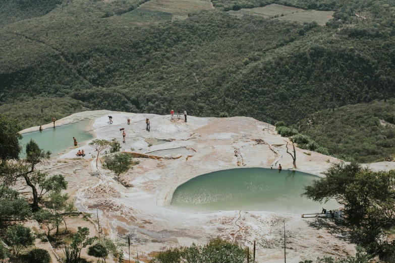 a group of people standing around a pool of water, by Elsa Bleda, pexels contest winner, shipibo, lush vista, grey, pools