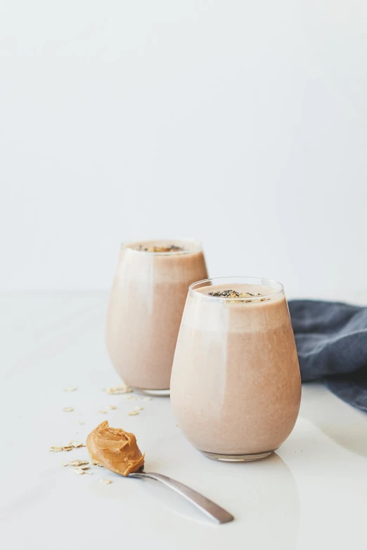 two glasses filled with smoothie next to a spoon, a portrait, unsplash, s'mores, set against a white background, milkshake, detailed product image