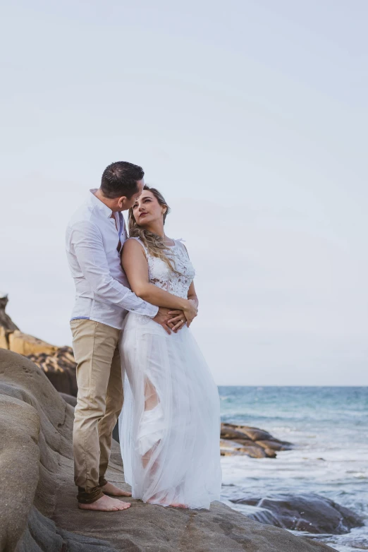 a man and a woman standing on a rock next to the ocean, white and gold robes, manly, hugging, pr shoot