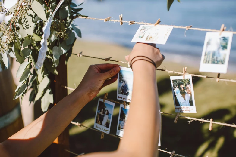 a woman is hanging pictures on a wire, a polaroid photo, unsplash, wedding, on the coast, hanging from a tree, cards