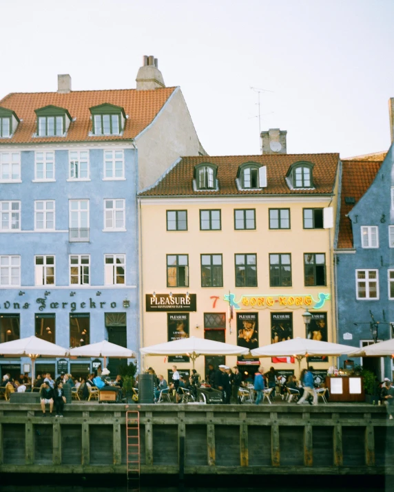 a row of buildings next to a body of water, a colorized photo, by Christen Dalsgaard, pexels contest winner, crowded square, instagram story, lgbtq, denmark