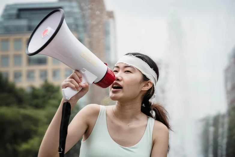 a woman holding a megaphone in front of a fountain, by Itō Seiu, pexels contest winner, hurufiyya, chinese woman, in a white tank top singing, avatar image, sports photo