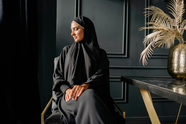 a woman in a black hijab sitting at a table, inspired by Modest Urgell, pexels contest winner, hurufiyya, religious robes, black furniture, a handsome, arabian