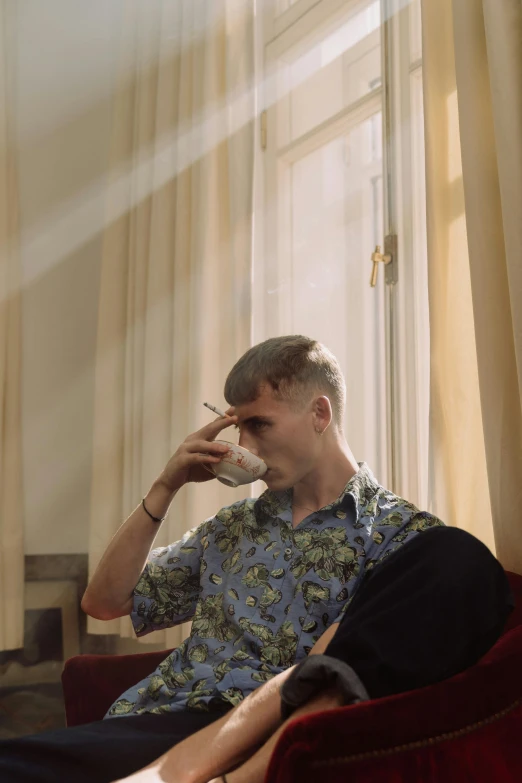 a man sitting in a chair talking on a cell phone, an album cover, inspired by Oskar Lüthy, trending on pexels, hyperrealism, bowl haircut, drinking tea, patterned clothing, sunlight