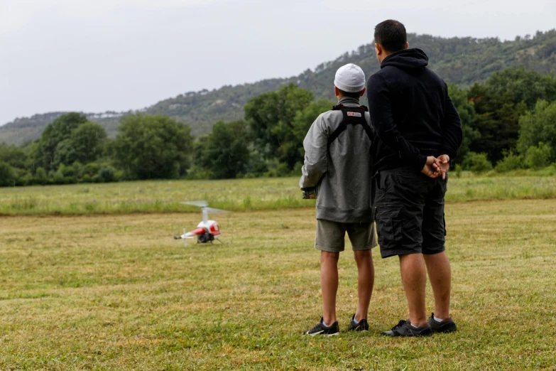 a couple of people that are standing in the grass, by Romain brook, on a landing pad, softair center landscape, teenage boy, view from a distance