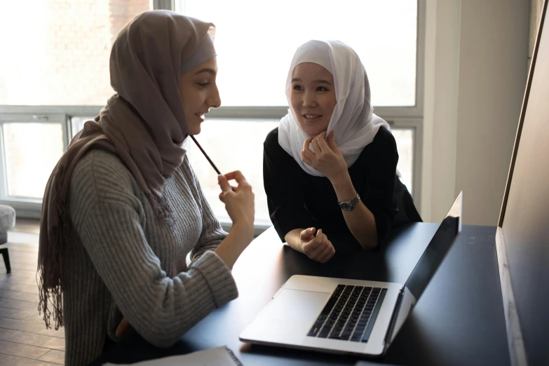 two women sitting at a table in front of a laptop, inspired by Maryam Hashemi, trending on pexels, hurufiyya, in a school classroom, asian human, wearing a head scarf, ismail inceoglu and ruan jia