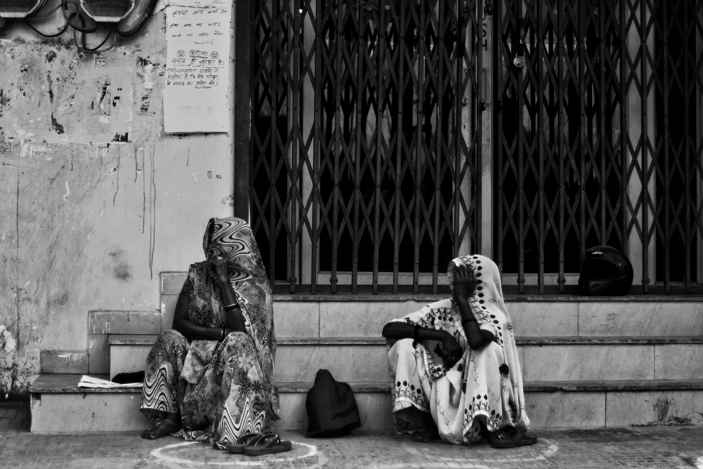 a couple of women sitting next to each other on a sidewalk, by Ahmed Yacoubi, poverty, intricate robes, black and white colors, hair covering eyes