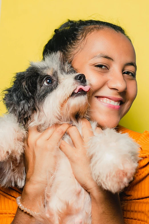 a woman holding a small dog in her arms, a portrait, by Olivia Peguero, shutterstock contest winner, on a yellow canva, mixed race, havanese dog, slide show