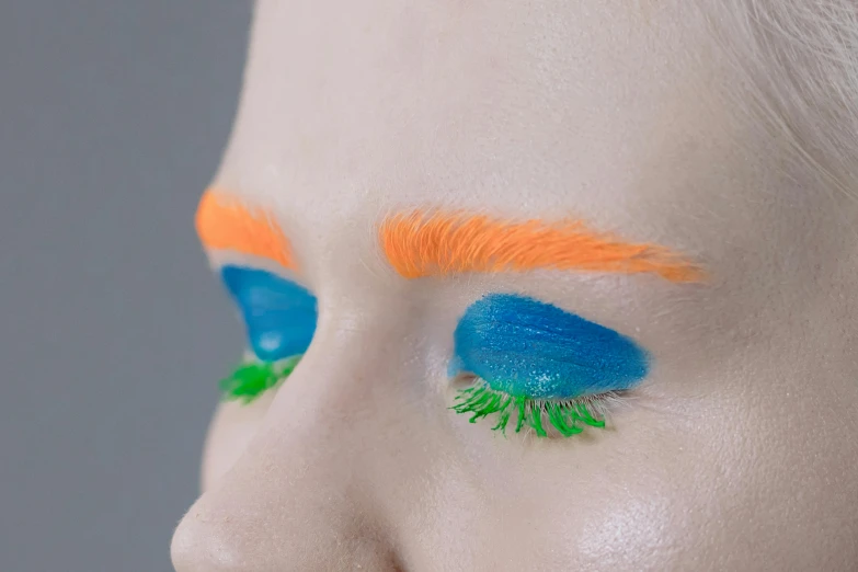 a close up of a person with blue and orange makeup, an album cover, inspired by Bert Stern, trending on pexels, conceptual art, bushy eyebrows, green and blue, aleksandra waliszewska, wearable art