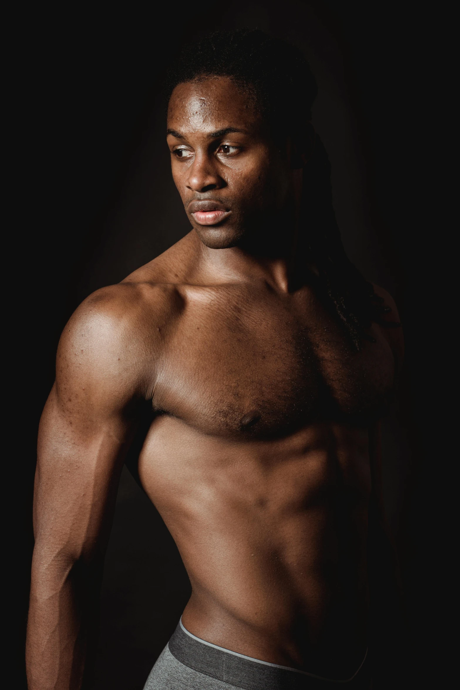 a shirtless man standing in front of a black background, inspired by Terrell James, strong young man, emmanuel shiru, aged 2 5, over his shoulder