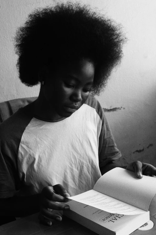 a woman sitting at a table reading a book, a black and white photo, pexels contest winner, black arts movement, afro hair, light skinned african young girl, ((portrait)), :: morning