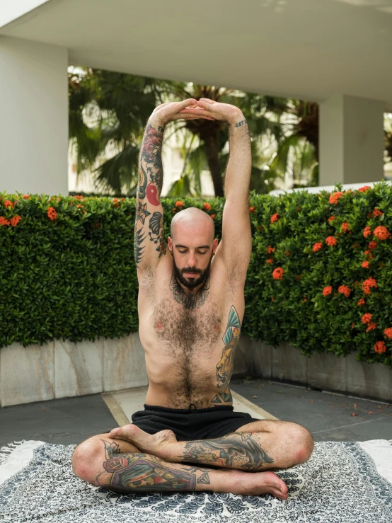 a man sitting in the middle of a yoga pose, a tattoo, with palm trees in the back, basil gogos, hairless, profile image