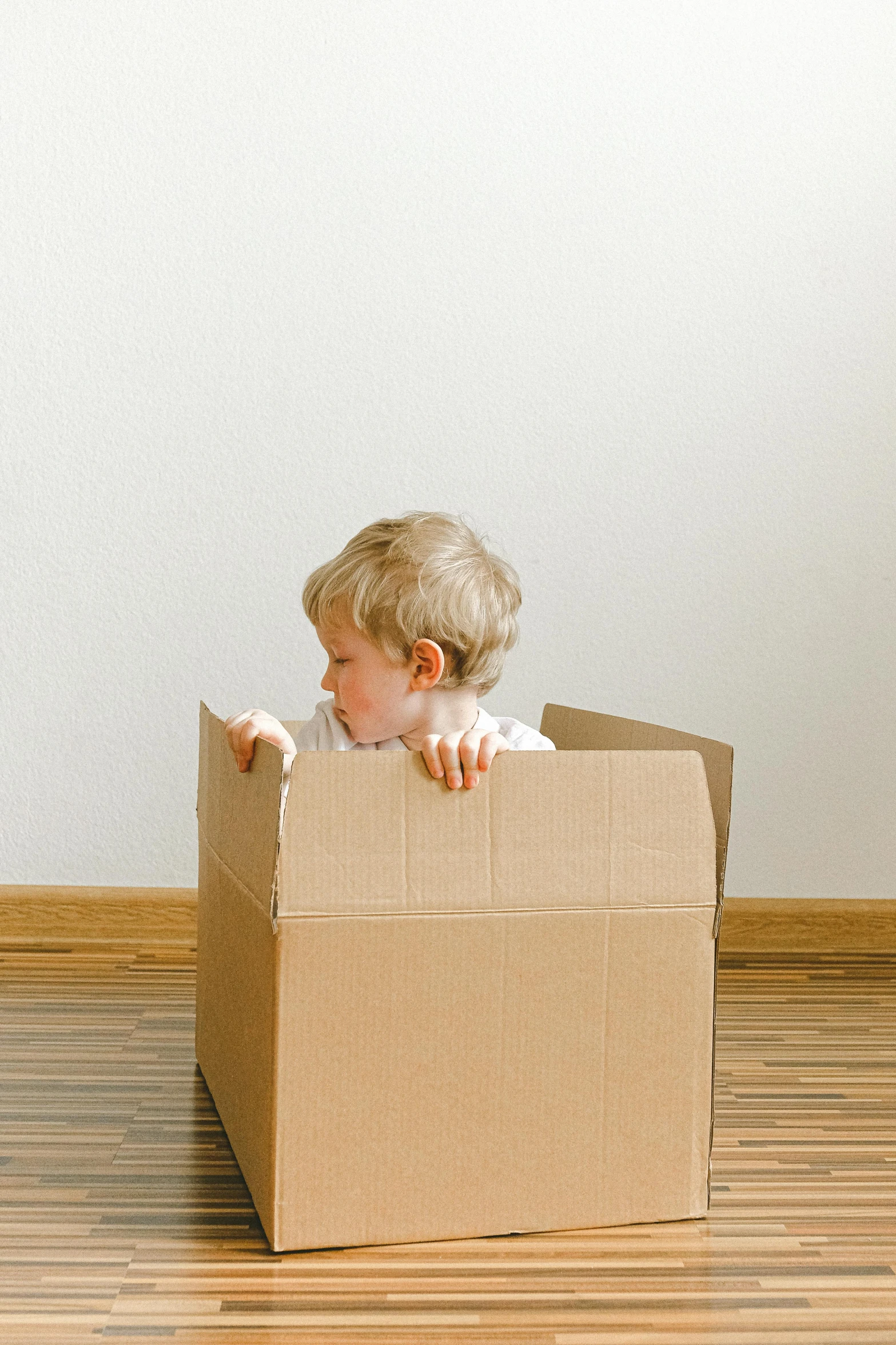 a small child sitting inside of a cardboard box, ecommerce photograph, sparse room, instruction, no - text no - logo