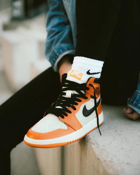 a person sitting on a ledge wearing a pair of sneakers, inspired by Jordan Grimmer, orange theme, zoomed out shot, “air jordan 1, shows a leg