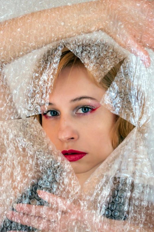 a woman holding a shower curtain over her head, an album cover, inspired by Anna Füssli, pixabay contest winner, cracked plastic wrap, with professional makeup, color photograph portrait 4k, looking into the camera