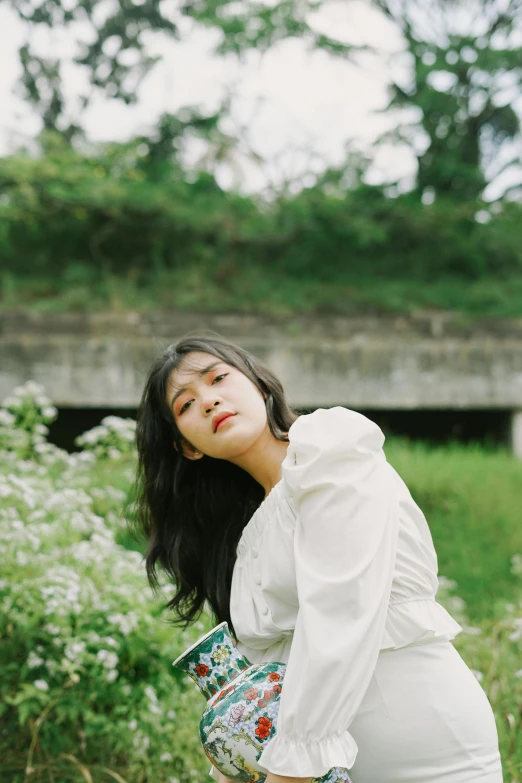 a woman standing in a field holding a purse, an album cover, inspired by Kim Jeong-hui, unsplash, wearing white clothes, bae suzy, portrait image, thoughtful )