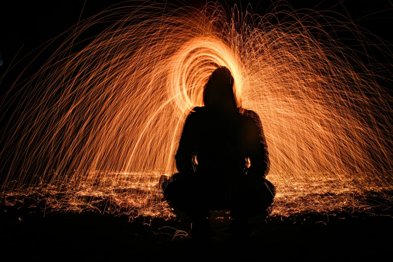 a person sitting in front of a fire, art photography, golden hour firefly wisps, outline glow, spiraling, the pyro