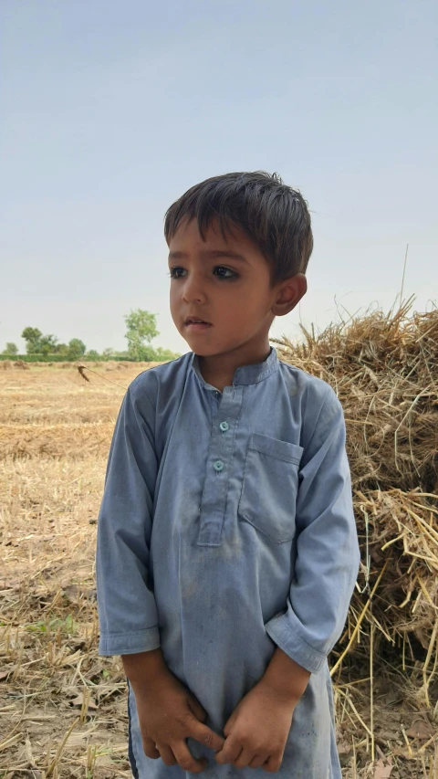 a young boy standing in front of a pile of hay, by Riza Abbasi, profile picture, malnourished, looks directly at camera, no crop