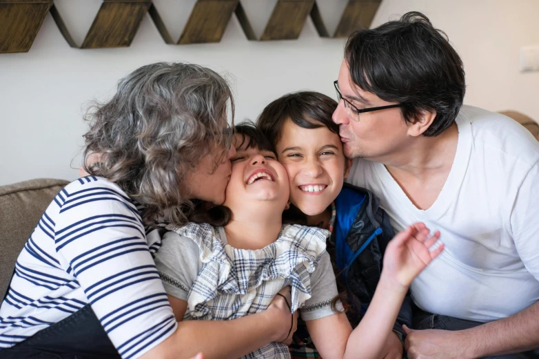 a woman sitting on top of a couch next to two children, by Lisa Milroy, pexels contest winner, kissing each other, andy milonakis, joyful people in the house, non-binary