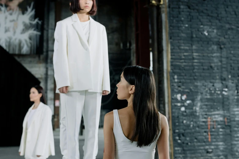 a woman sitting on the ground in front of a group of people, inspired by Vanessa Beecroft, pexels contest winner, minimalism, wearing futuristic white suit, 3 sisters look into the mirror, a young asian woman, [ theatrical ]