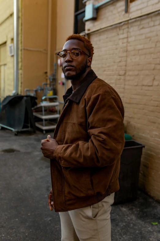 a man standing in the middle of a street, an album cover, trending on pexels, brown jacket, mkbhd, thoughtful pose, man with glasses