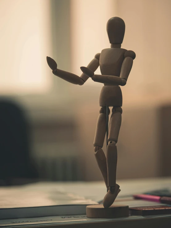 a wooden mannequin standing on top of a desk, unsplash, figurative art, articulated joints, toy photo, dancing character, back of hand on the table