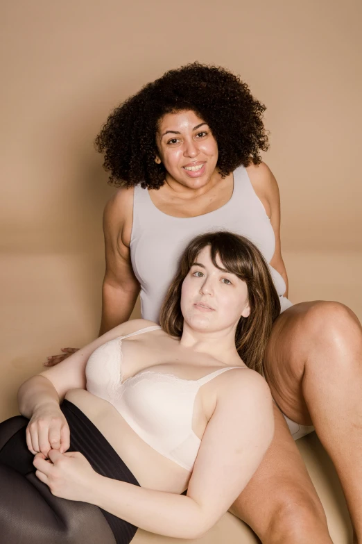 a couple of women sitting on top of a bed, plus-sized, natural skin tones, wearing bra, on display