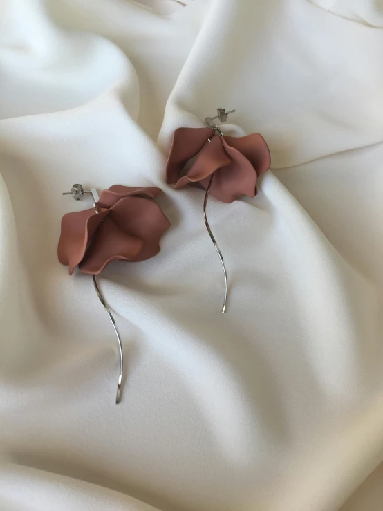 a pair of earrings sitting on top of a white cloth, a colorized photo, by Emma Andijewska, unsplash, long petals, taupe, 3 dimensional, featuring rhodium wires