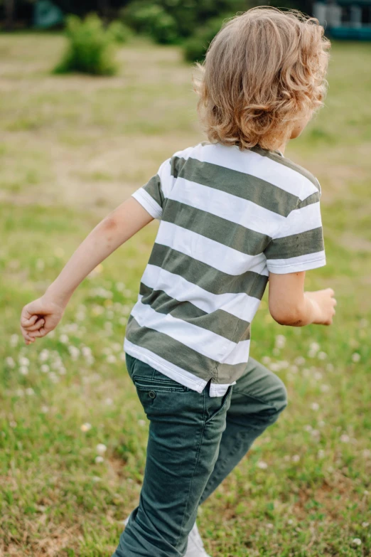 a young boy riding a skateboard on top of a lush green field, by David Simpson, unsplash, striped shirt, printed on a cream linen t-shirt, walking away, sprinting