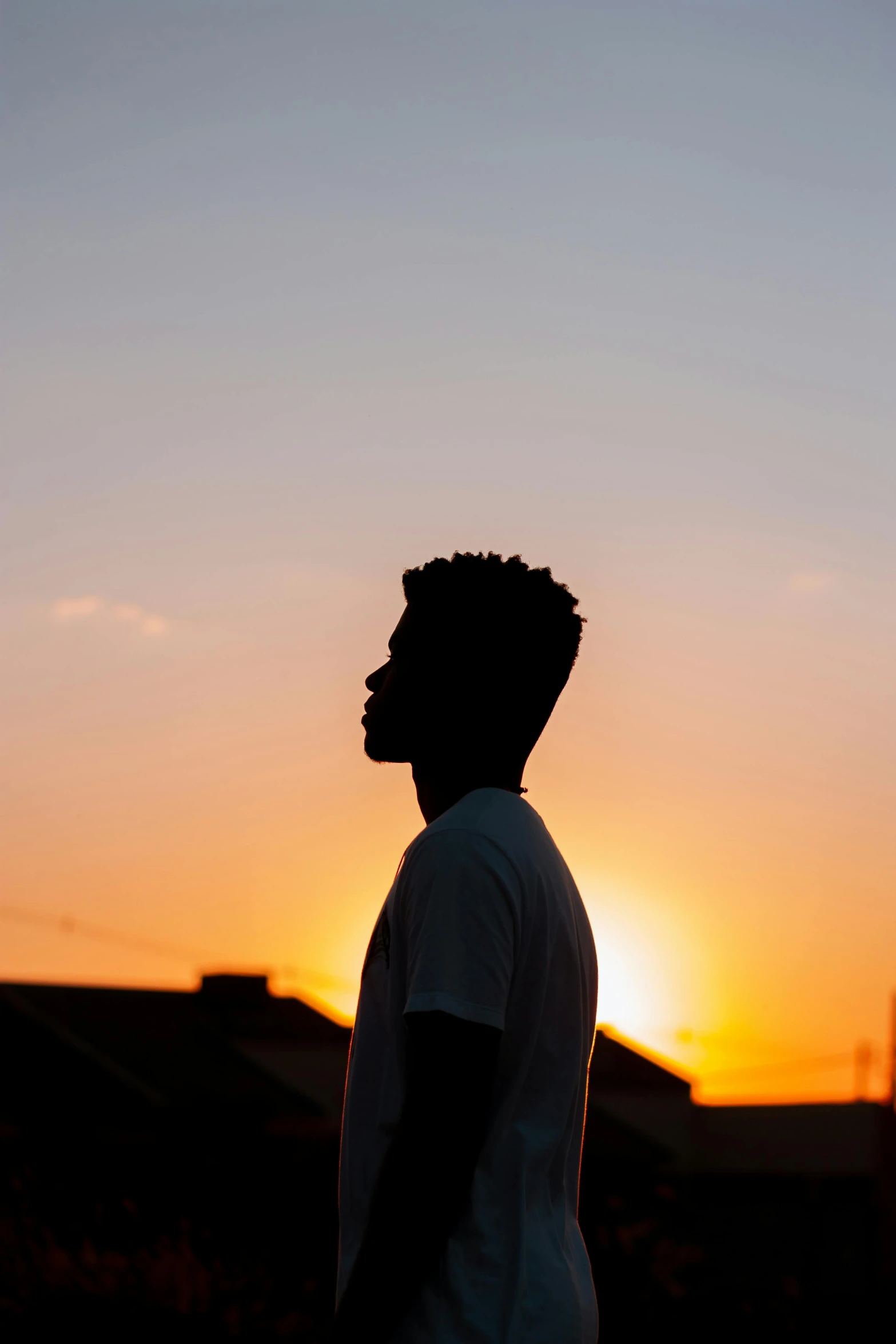 a silhouette of a man standing in front of a sunset, an album cover, pexels contest winner, black teenage boy, profile portrait, shot from roofline, an all white human